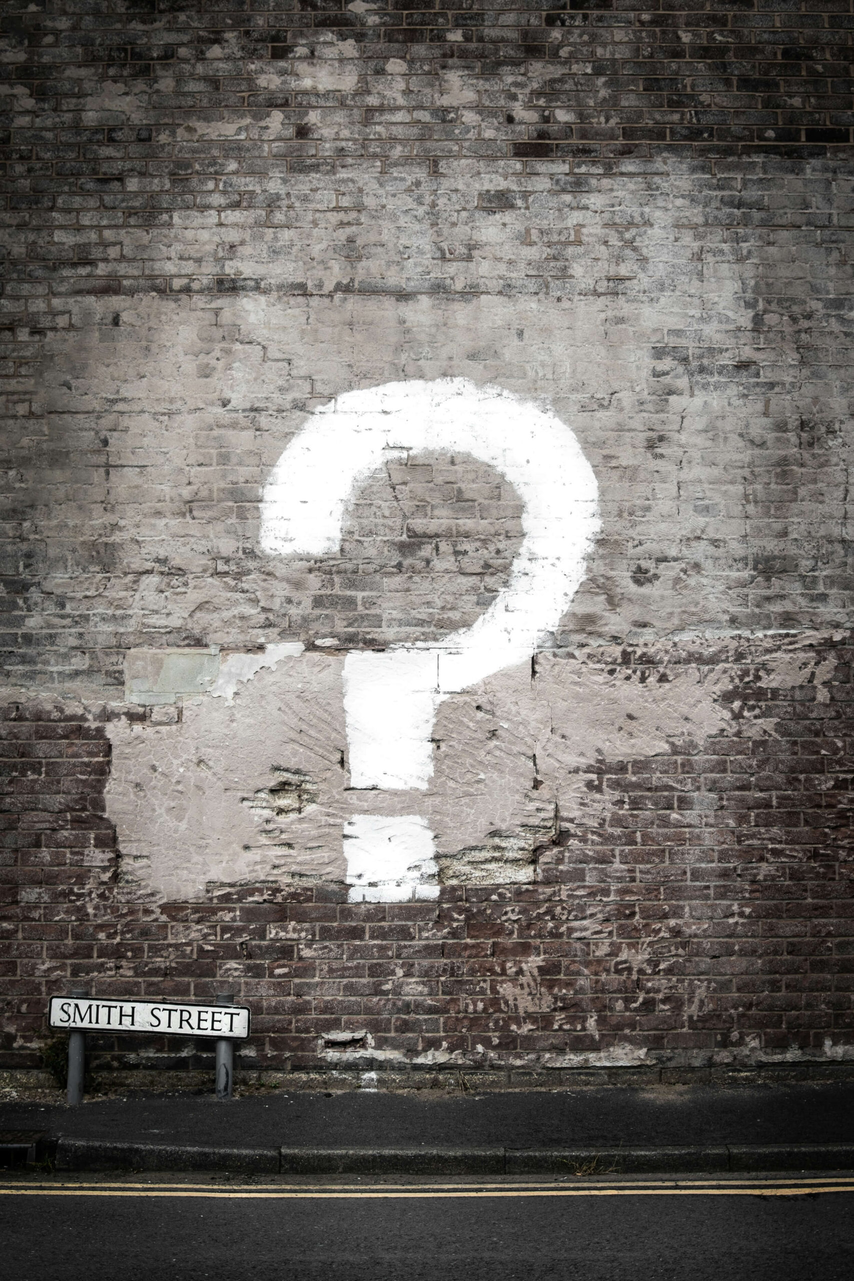 A large white question mark painted on an aged brick wall on Smith Street, suggesting a sense of mystery or the search for answers in an urban setting.
