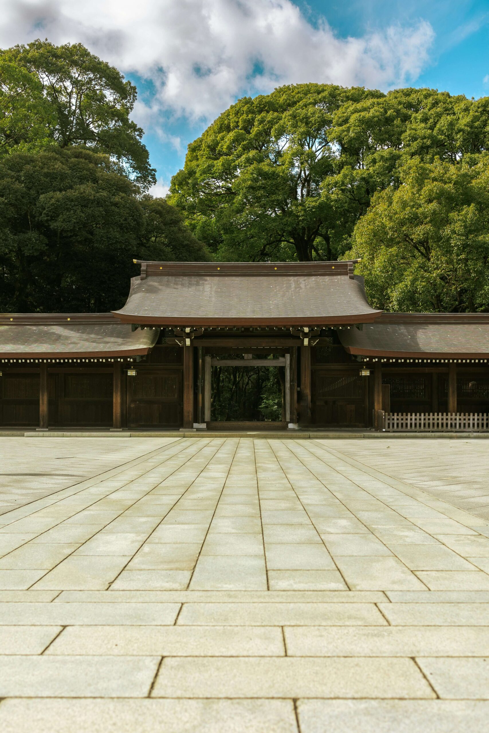 The expansive stone-paved approach leading to the main entrance of Meiji Shrine, framed by a verdant backdrop of towering trees.
