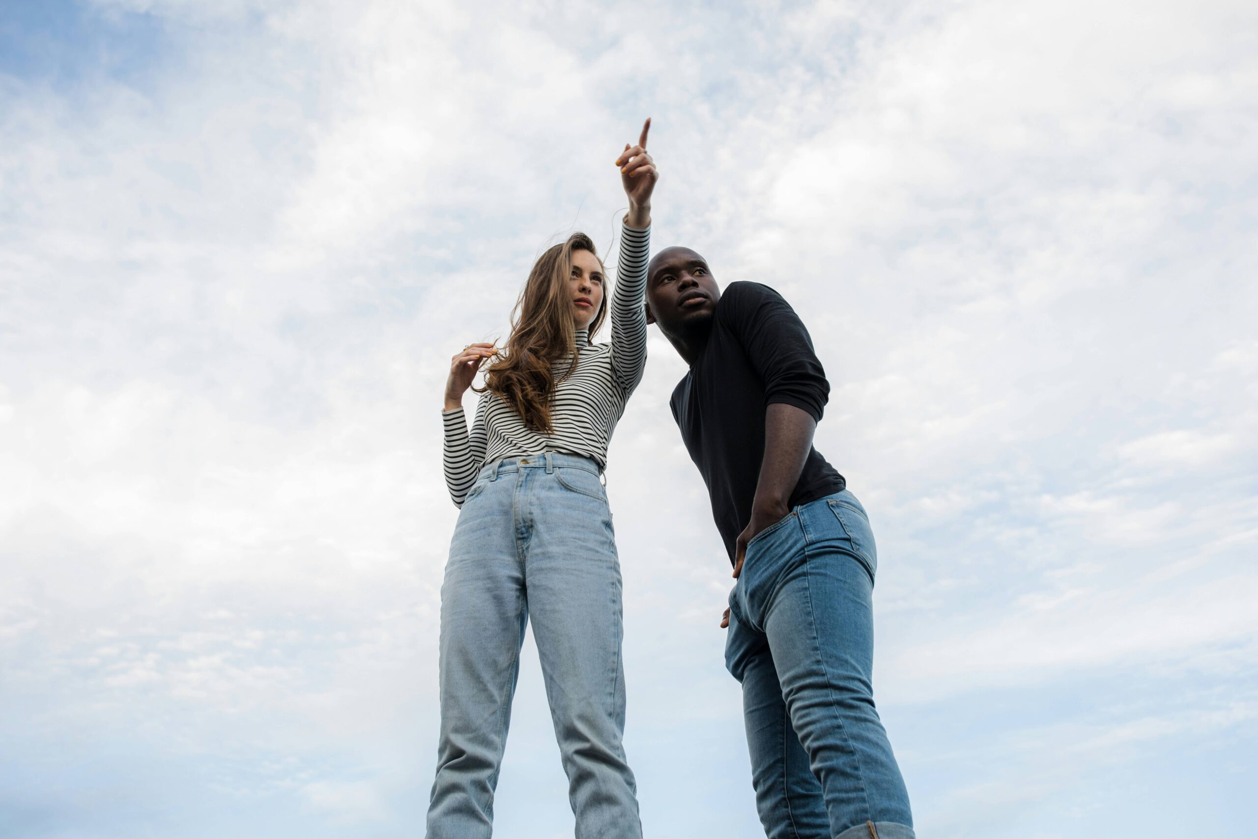 Alt Two people standing against a cloudy sky background, with one person pointing upwards, illustrating the action of pointing out a location
