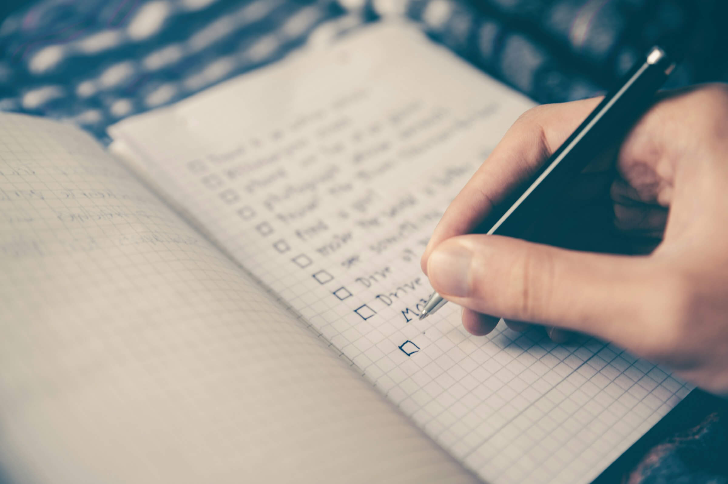 A hand writing in a notebook with a pen, creating a checklist or schedule. This image illustrates the use of the -て form to describe two activities in Japanese, often used when planning or writing schedules.
