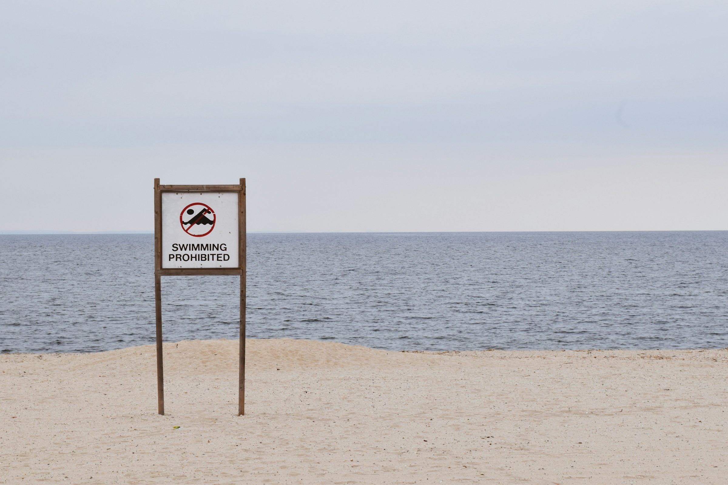 A sign on a beach with the text "SWIMMING PROHIBITED" and an image of a swimmer with a red line through it. This image represents the Japanese grammatical structure "-てはいけません" (- te wa ikemasen), which is used to indicate that an action is not allowed.
