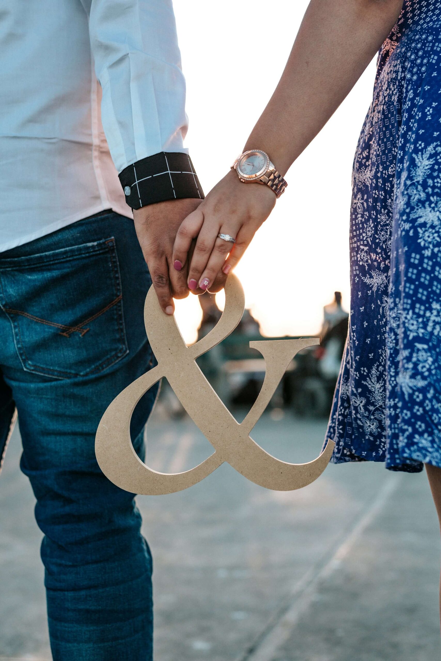 This image shows a man and a woman holding hands while holding a wooden ampersand (&) symbol. This image illustrates one of the uses of Genki Grammar #25 (と), specifically the "together with" usage.
