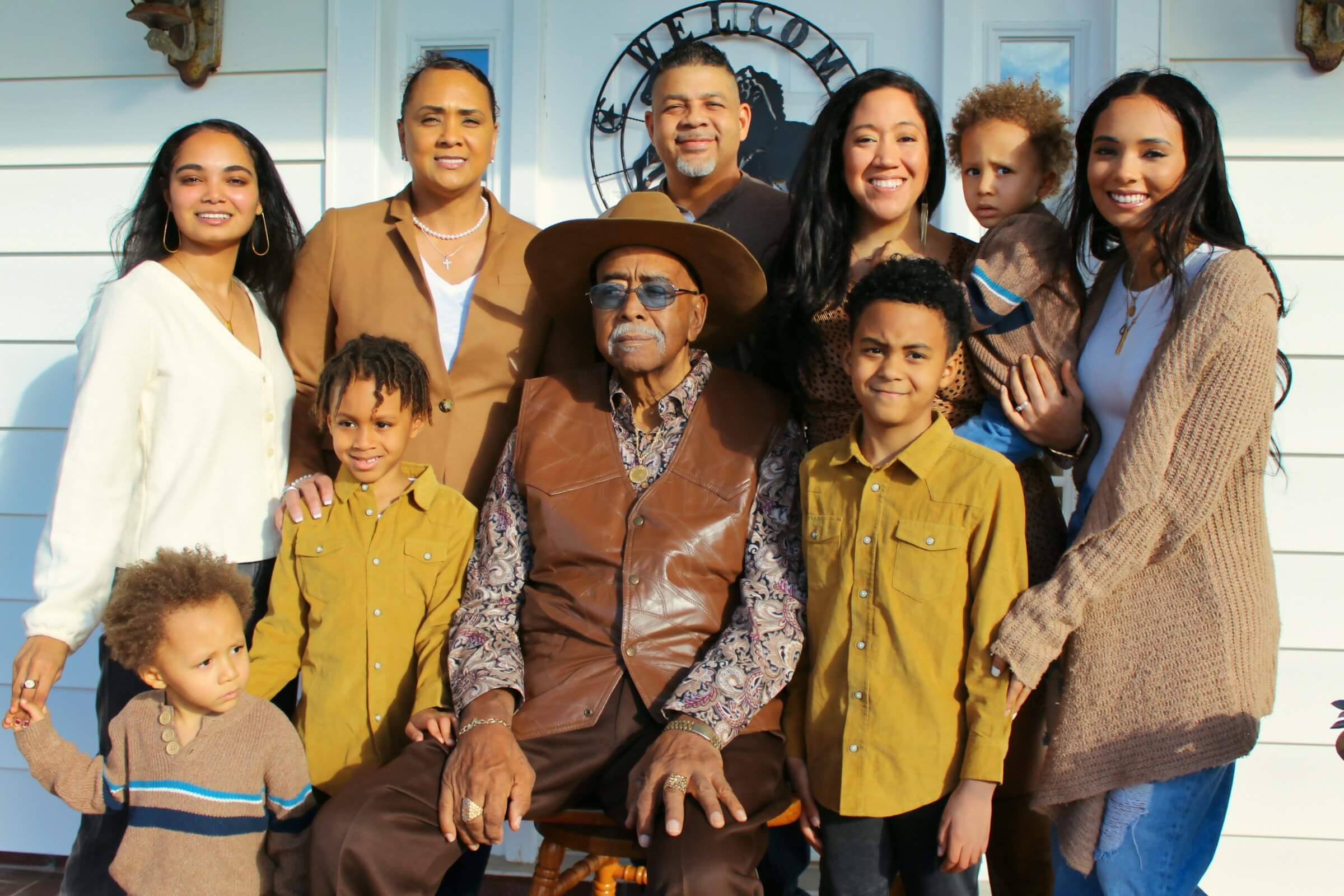 A diverse, multi-generational family standing together outside their home, featuring grandparents, parents, and children smiling warmly, representing family terms and relationships.
