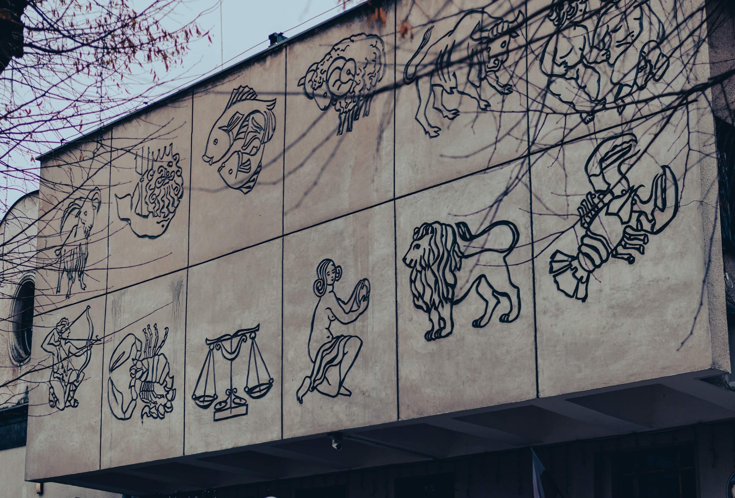 This image displays a series of Western zodiac signs represented as artistic line drawings on a building's facade. These symbols, which include various animals and figures like a fish, lion, and scales, provide a visual connection to the Japanese 干支 (Eto) system by illustrating a different cultural approach to astrological signs.  