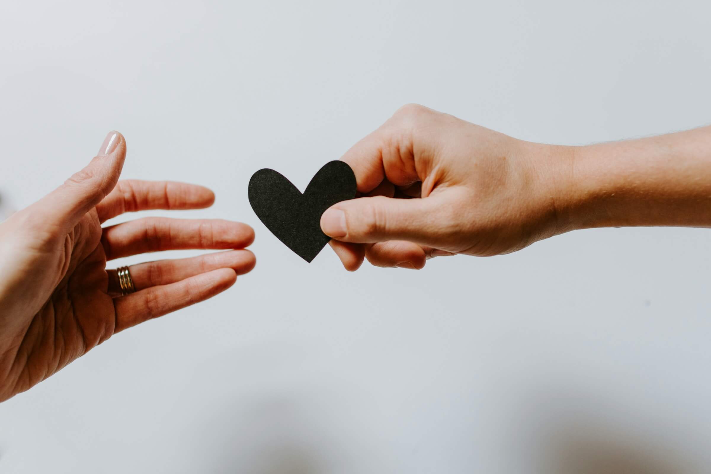 Close-up of two hands, one holding and offering a small black heart-shaped object to the other. This image represents the concept of wanting or desiring something, illustrating the use of the Japanese word "ほしい" (hoshii).
