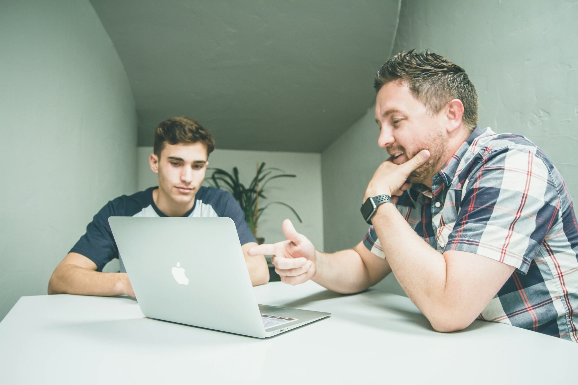 Two people sitting at a table with a laptop, one person pointing at the screen while giving a suggestion to the other. This image represents a situation where the phrase "-taradoudesuka" is being used to offer advice or a suggestion.
