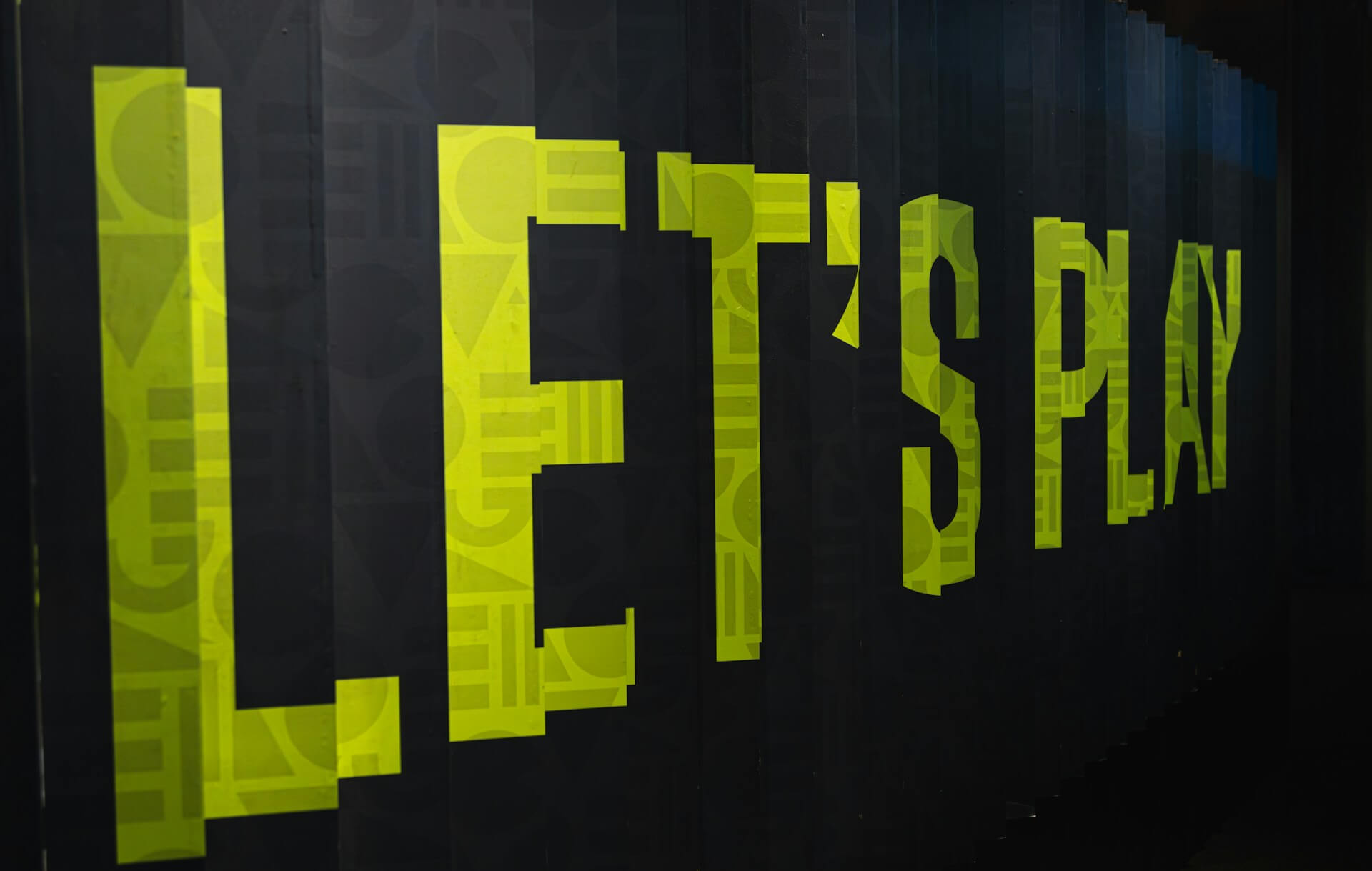 Bright yellow text on a dark background that reads "LET'S PLAY." This image represents the concept of the Volitional Form in Japanese, which is used to suggest doing something together, similar to the English phrase "Let's."
