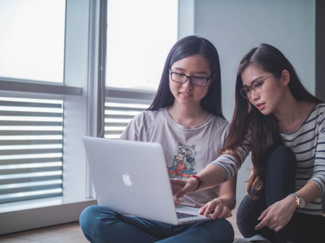 A woman pointing at a laptop, saying 'Koko wa chotto chigau yo ne' to indicate something is slightly different. This image illustrates the use of 'ne' in Japanese.
